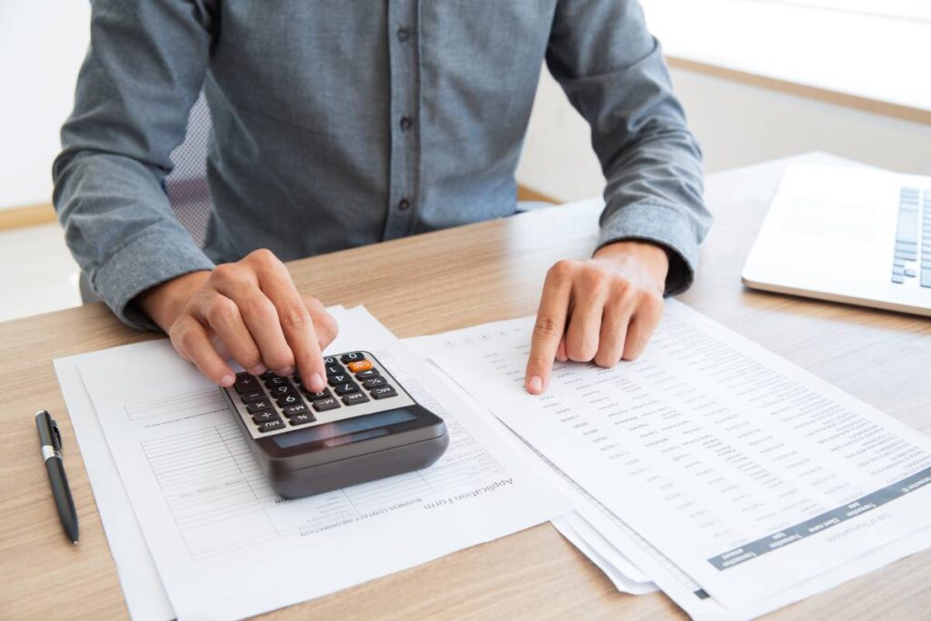 homem com papeis na mesa fazendo cálculo na calculador