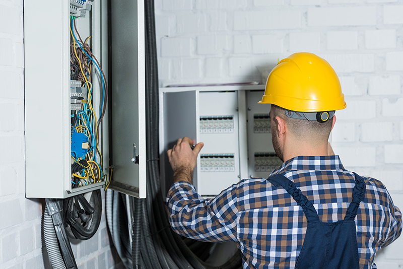 Profissional eletricista de costas abrindo quadro de luz